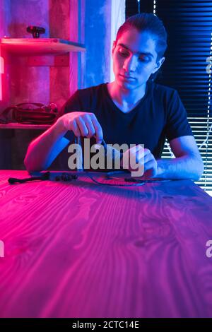 Artigiano fa dreamcatcher di accessori da cucire in officina scura illuminato da luce al neon, spazio di copia. Foto Stock
