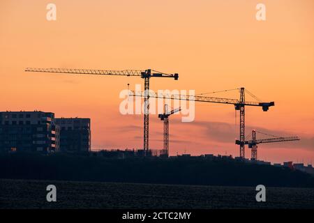 Attività di costruzione sul sito di costruzione. Sagome di gru contro il cielo dorato. Foto Stock