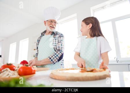 Foto di nipote di bambina passare il tempo con nonno invecchiato parlare mettere salsa di pomodoro su pasta famiglia pizza ricetta cottura cucinare insieme Foto Stock