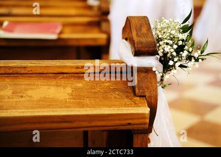 panchine in chiesa decorata con fiori bianchi e tessuti per un matrimonio Foto Stock