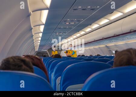 Stewardess in maschera chirurgica e giallo ovest dando istruzioni ai passeggeri. Mezzo aereo vuoto a causa della pandemia COVID. Foto Stock