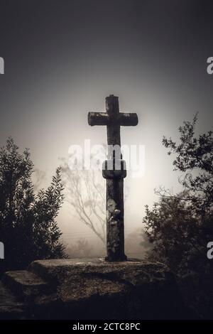 Scatto di una bella croce di pietra religiosa su una nebbia giorno Foto Stock