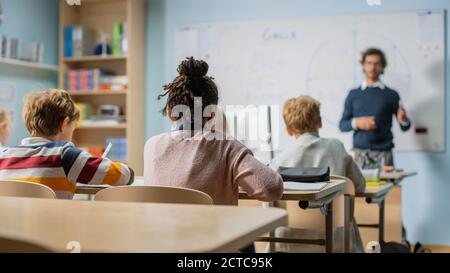 Insegnante entusiasta spiega le lezioni e fa le domande da un'aula piena di bambini variegati luminosi. Nel gruppo scolastico elementare di Smart Foto Stock