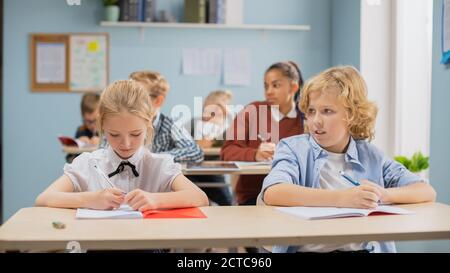 Classe elementare di diversi Bright Children ascoltando attentamente il loro insegnante che dà lezione. I capretti brillanti nella scrittura della scuola nell'esercitazione Foto Stock