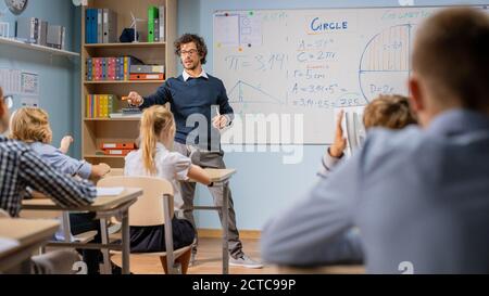 Insegnante entusiasta spiega le lezioni e fa le domande da un'aula piena di bambini variegati luminosi. Nel gruppo scolastico elementare di Smart Foto Stock