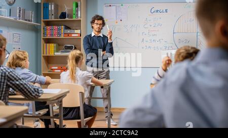 Insegnante entusiasta spiega le lezioni e fa le domande da un'aula piena di bambini variegati luminosi. Nel gruppo scolastico elementare di Smart Foto Stock