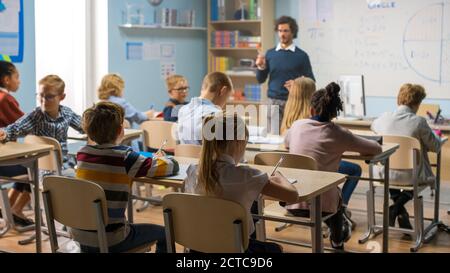 L'insegnante premuroso spiega la lezione a un'aula piena di bambini variegati e luminosi. In scuola elementare con Gruppo di Smart Multi-etnic Kids Learning Foto Stock