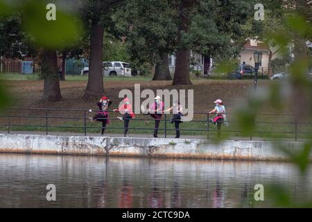 4 donne asiatiche americane in maschere chirurgiche allungano le gambe in una foto scattata attraverso il fogliame e accros un lago. A Queens, New York City.. Foto Stock