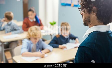 Sopra il colpo dell'anima dell'insegnante che spiega la lezione alla classe piena dei bambini luminosi differenti, nel gruppo della scuola elementare dei capretti multietnici intelligenti Foto Stock