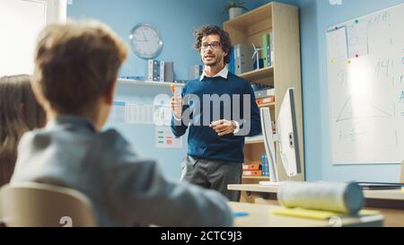 Insegnante entusiasta spiega la lezione a un'aula piena di bambini variegati e conduce la lezione con fare domande. Nel gruppo della scuola elementare di Foto Stock