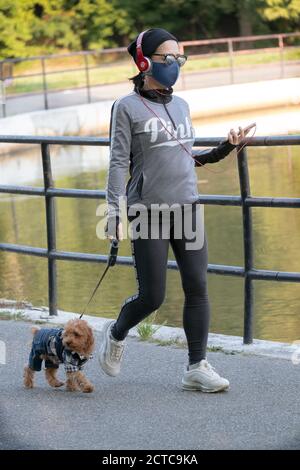 Una donna fuori per una camminata di esercitazione con il suo cane che sta portando un costume della camicia del plaid & dei pantaloni del denim. In Queens, New York City. Foto Stock