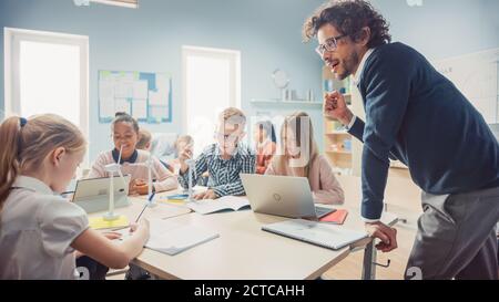 Nella scuola elementare: Classe di giovani bambini intelligenti lavorano come un team che utilizza i computer tablet per programmare le turbine eoliche. In aula con i bambini che imparano Foto Stock