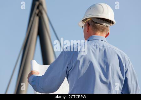 Architetto o ingegnere che legge un piano di costruzione di fronte sfondo industriale - focus sulla testa Foto Stock
