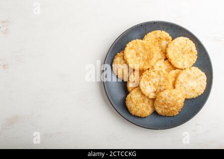 Biscotti tradizionali giapponesi di patatine di riso con salsa di miele e soia su un piatto di ceramica blu su fondo di legno bianco. Vista dall'alto, disposizione piatta, spazio per la copia. Foto Stock