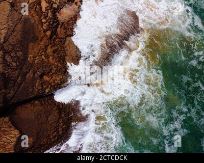 Vista aerea dall'alto delle onde marine che colpiscono le rocce sulle scogliere. Onde di mare schiumose che si infrangono sulla costa Foto Stock