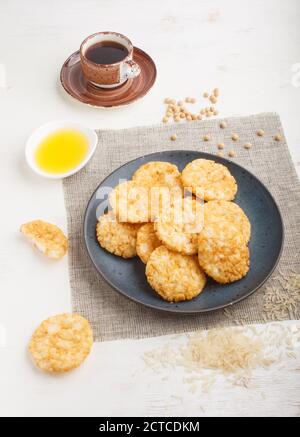Biscotti tradizionali giapponesi di patatine di riso con salsa di miele e soia su un piatto di ceramica blu e una tazza di caffè su uno sfondo di legno bianco. Vista laterale, Foto Stock