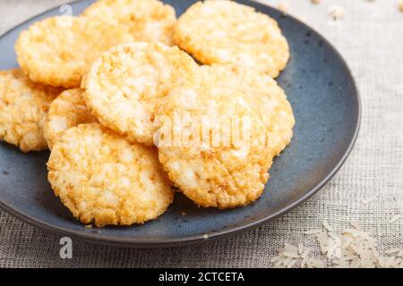 Biscotti tradizionali giapponesi di patatine di riso con salsa di miele e soia su un piatto di ceramica blu su un fondo tessile di lino. Vista laterale, primo piano, selettivo Foto Stock