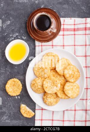 I tradizionali biscotti giapponesi di patatine di riso con salsa di miele e soia su un piatto bianco di ceramica e una tazza di caffè su fondo nero di cemento. Vista dall'alto Foto Stock