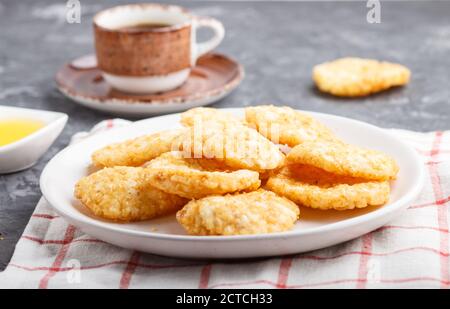 Biscotti tradizionali giapponesi di patatine di riso con salsa di miele e soia su un piatto bianco di ceramica e una tazza di caffè su un fondo nero di cemento. Vie laterali Foto Stock