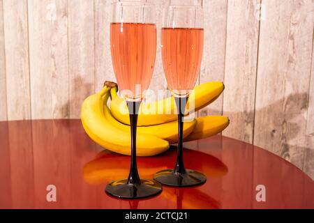 due bicchieri di spumante rosa accanto alle banane sul tavolo rosso Foto Stock