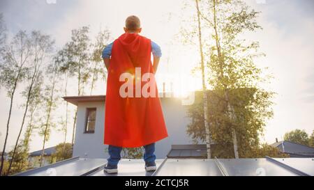 Ragazzo sta giocando un ruolo di Super Hero. Sta in piedi su un tetto di una casa con le mani sulla sua vita. Young Man indossa un capo rosso brillante. È Foto Stock