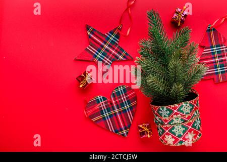 Vista dall'alto su sfondo rosso con un piccolo albero di Natale e decorazioni in forma di cuori, alberi di Natale e stelle per le vacanze di Natale. Foto Stock