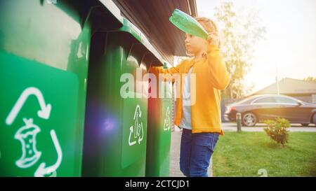 Giovane ragazza sta gettando via una bottiglia vuota di plastica in un cestino. Utilizza il corretto Garbge Bin perché questa famiglia sta smistando gli sprechi e sta aiutando a. Foto Stock