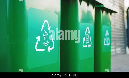 Bidoni per rifiuti in plastica di colore verde, con diversi loghi di riciclo sulla parte anteriore, impilati in fila contro la parete di legno marrone. Concetto di smistamento dei rifiuti per gli alimenti Foto Stock