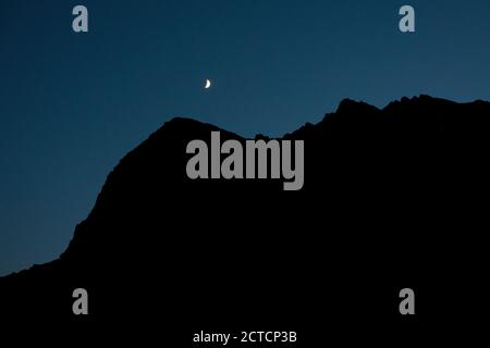 Luna di Crescent con silhouette di cresta di montagna contro cielo chiaro di notte Foto Stock