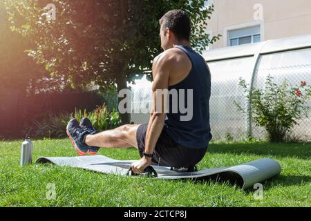 Una sessione di cross-training di un adolescente in abbigliamento sportivo utilizzando i rinforzi muscolari e. rinforzare le braccia e l'addome su un tappeto nel cortile in una giornata di sole Foto Stock