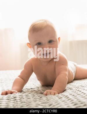 Un bambino di quattro mesi giace sullo stomaco e guarda la macchina fotografica. Un bambino sorride Foto Stock