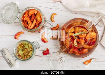 Tisane vitaminiche. Deliziosa e sana bevanda calda autunnale a base di mele secche e Linden in una teiera di vetro su un tavolo bianco. Messa a fuoco selettiva Foto Stock