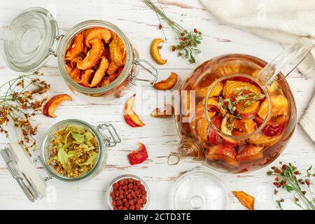 Tisane vitaminiche. Deliziosa e sana bevanda calda autunnale a base di mele secche, Linden, Rowan, fragole selvatiche in una teiera di vetro su un tavolo bianco Foto Stock