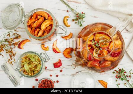 Tisane vitaminiche. Deliziosa e sana bevanda calda autunnale a base di mele secche, Linden, Rowan, fragole selvatiche in una teiera di vetro su un tavolo bianco Foto Stock