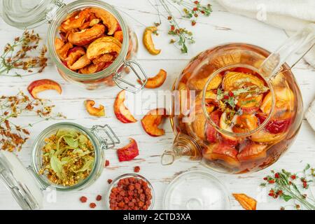Tisane vitaminiche. Deliziosa e sana bevanda calda autunnale a base di mele secche, Linden, Rowan, fragole selvatiche in una teiera di vetro su un tavolo bianco Foto Stock