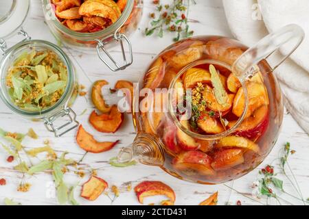 Tisane vitaminiche. Deliziosa e sana bevanda calda autunnale a base di mele secche, Linden, fragole selvatiche in una teiera di vetro su un tavolo bianco. Sele Foto Stock