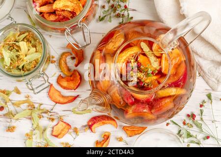 Tisane vitaminiche. Deliziosa e sana bevanda calda autunnale a base di mele secche, Linden, fragole selvatiche in una teiera di vetro su un tavolo bianco. Sele Foto Stock