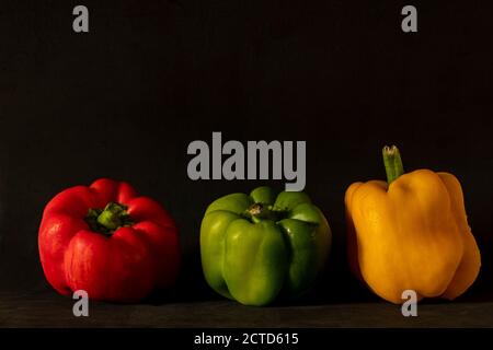 primo piano di tre peperoni: rosso, verde e giallo su sfondo scuro Foto Stock