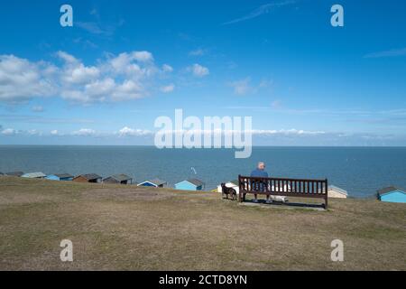Whitstable, UK - 6 settembre 2020 UN uomo anziano si siede su una panchina che guarda verso il mare a Tankerton, Whstable. Ha due cani con lui. C'è una riga di b Foto Stock