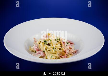 Carbonara con pancetta e basilico su un piatto. Vista dall'alto piatta su piastra bianca su sfondo blu. Foto Stock