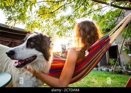 donna con cane che si rilassa in amaca nel cortile posteriore Foto Stock