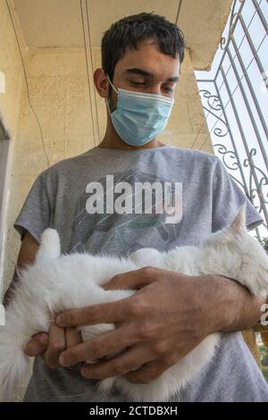 Il giovane indossa una maschera per proteggere il viso lui e lui porta il gatto Foto Stock