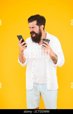 arrabbiato uomo maturo bearded gridare emozionalmente sul telefono mentre beve il caffè del mattino, esprimendo la rabbia. Foto Stock