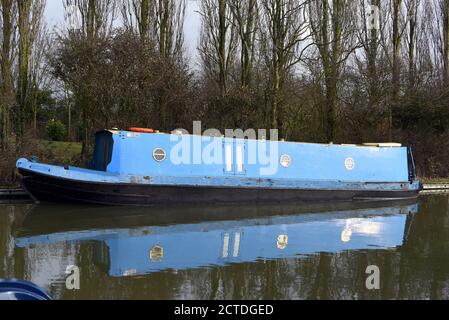 In questa foto scattata lungo il canale Grand Union nel Buckinghamshire, si riflette una barca blu che si trova in acque fisse Foto Stock