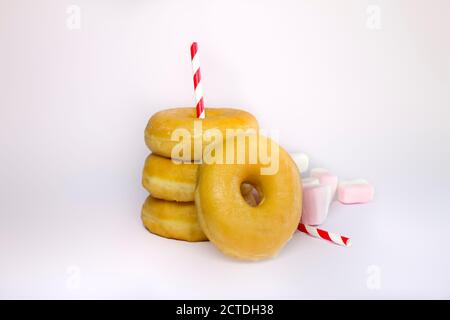 Quattro ciambelle o ciambelle classiche Stack con Marshmallows e due Straw Red Stripe su uno sfondo bianco. Foto Stock