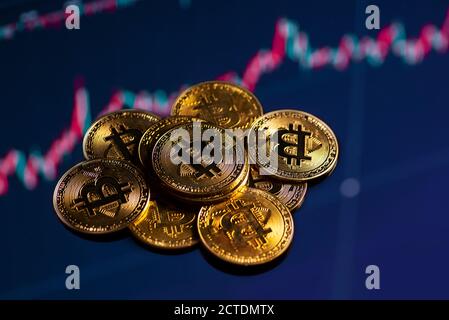 Primo piano di monete d'oro bitcoin su uno sfondo grafico di trading in corso. Foto Stock