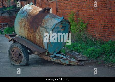 Vecchio rimorchio per autocisterna arrugginito sullo sfondo della parete di mattoni. Foto Stock