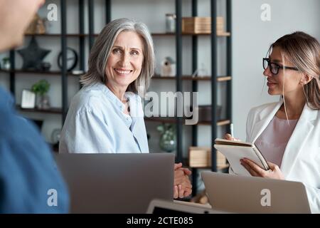 Sorridente insegnante di mentore femminile matura che comunica con studenti o stagisti. Foto Stock