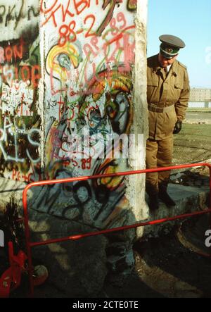 Un Oriente poliziotto tedesco guarda ad un piccolo albero di Natale che ornano il tedesco-occidentale della parte del muro di Berlino. La protezione è in piedi al creato di recente apertura nel muro di Berlino a Potsdamer Platz. Foto Stock