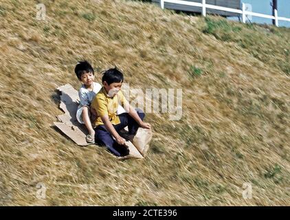 1975 - Bambini scorrere su una collina a una temporanea struttura alloggiativa per rifugiati vietnamiti. Foto Stock